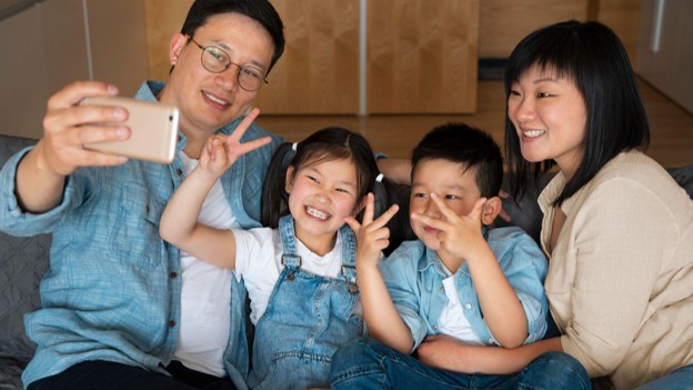 Keluarga beranggotakan ayah, ibu, dan dua anak sedang berfoto selfie bersama untuk media sosial.